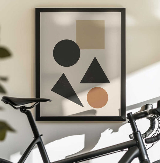 Minimalist geometric composition 07 by Little Dean, black-framed artwork above a bicycle; black triangles and a black circle with a tan square and brown circle on cream.
