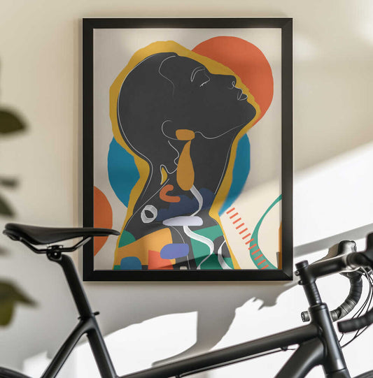 Modern Abstract Woman1 by City Art, black-framed artwork above a bicycle; an upward-facing dark profile surrounded by orange, yellow, teal and flowing abstract shapes.