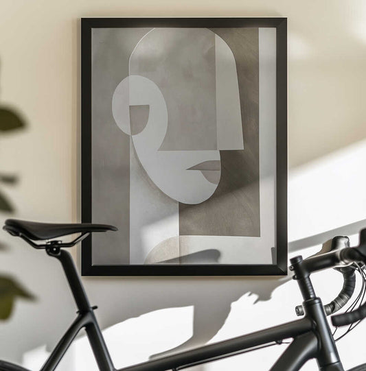 Neutral Portrait by SHANDU, black-framed artwork above a bicycle; a simplified face built from pale curved planes and taupe rectangular forms.