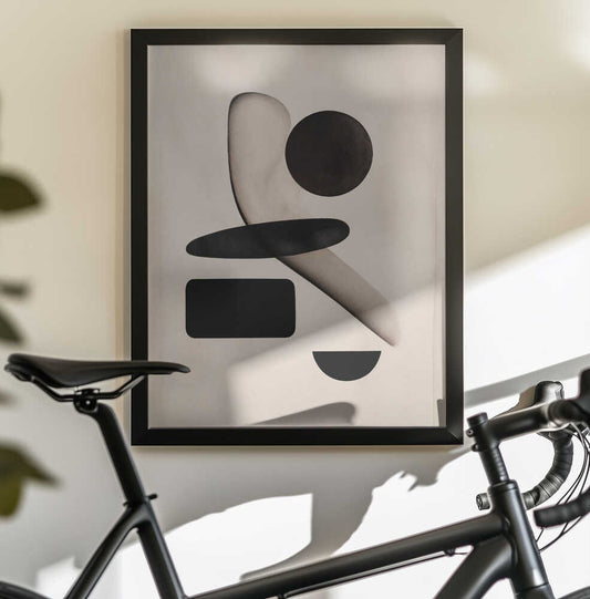 Shapeshift Harmony by THE MIUUS STUDIO, black-framed artwork above a bicycle; black geometric forms overlapping a soft curved beige ribbon.