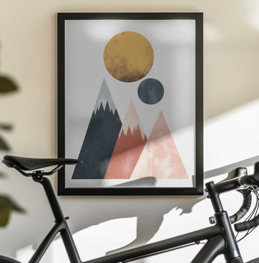Two Moons by SHANDU, black-framed artwork above a bicycle; three geometric mountain peaks beneath a gold-toned disc and a smaller dark moon.