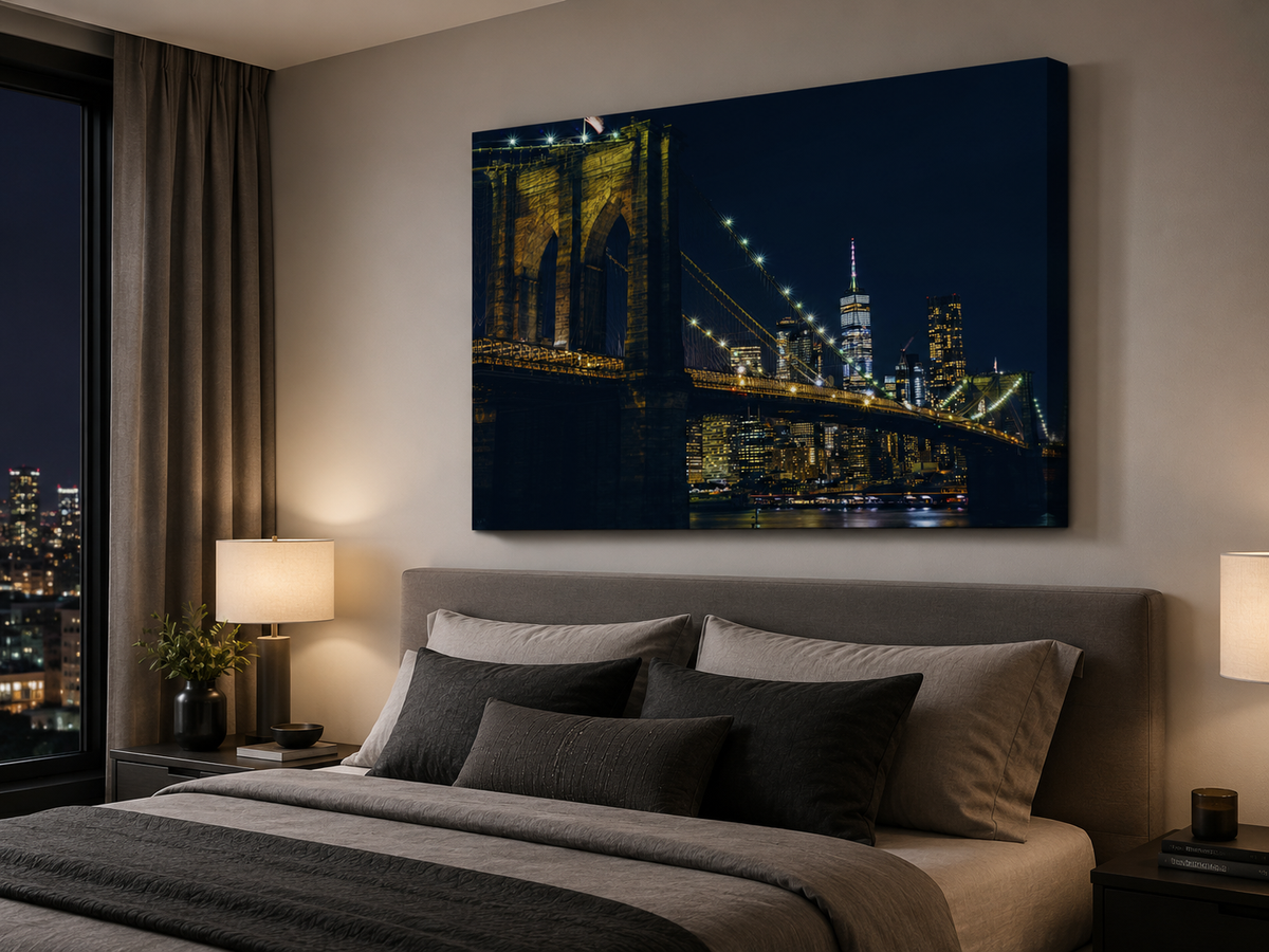 A large rectangular wall art print showing a nighttime city skyline with illuminated bridges and skyscrapers, displayed above a bed in a modern bedroom.