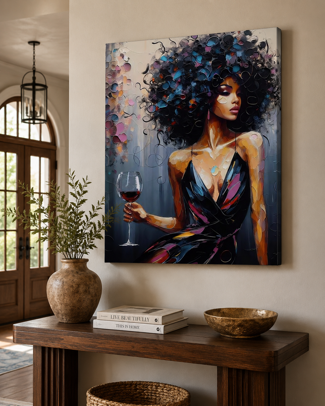 A large canvas wall art print depicting a woman with voluminous dark curly hair holding a glass of red wine, displayed on a beige wall above a wooden console table in a styled interior.