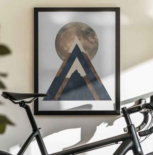 Bronze Moon by SHANDU, black-framed artwork above a bicycle; a bronze-toned moon behind layered dark triangular mountain forms.