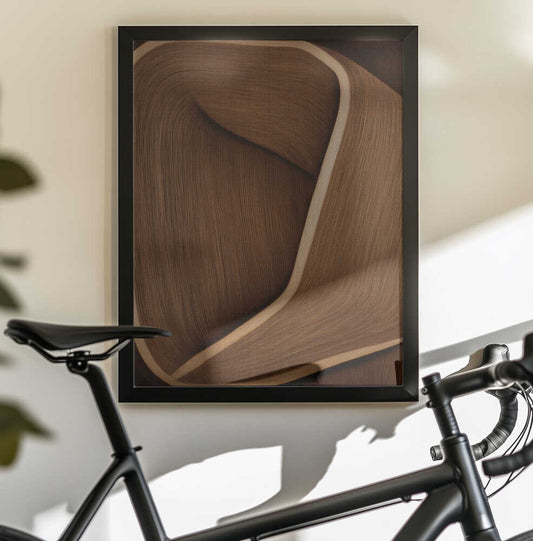 Caramel lines II by Alma, black-framed artwork above a bicycle; a twisting brown ribbon-like form with a pale raised edge and fine linear texture.