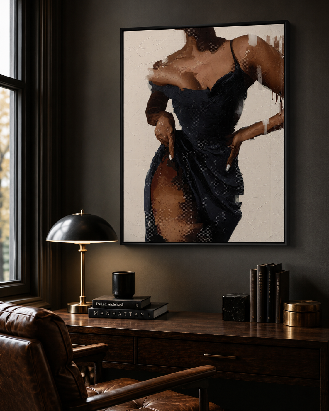 A framed vertical art print depicting a woman in a dark navy dress against a cream background, displayed on a dark wall above a wooden desk with a lamp and books in a moody room setting.