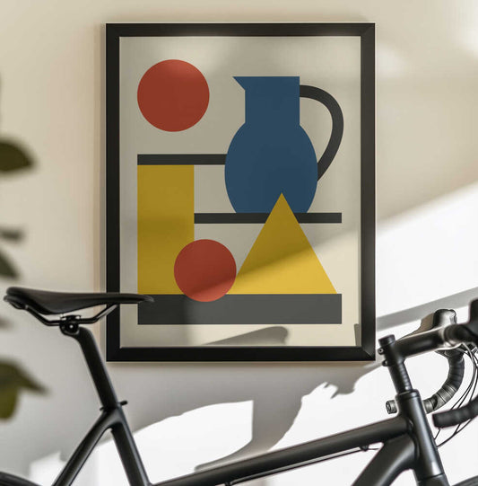 Geometric Shapes and Pitcher by Little Dean, in a black frame above a bicycle; a blue pitcher with red circles, yellow geometric shapes and black lines on cream.