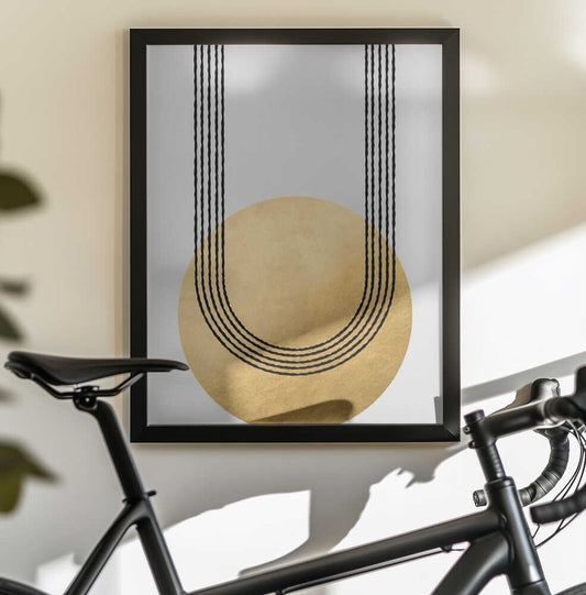 Gold balance by Rosana Laiz Blursbyai, black-framed artwork above a bicycle; gold-toned circle beneath parallel black curved lines.