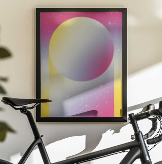 Minimal Pastel Cosmos by Amy Louise Baker, black-framed artwork above a bicycle; pastel sphere floating in a pink and yellow starry arch.