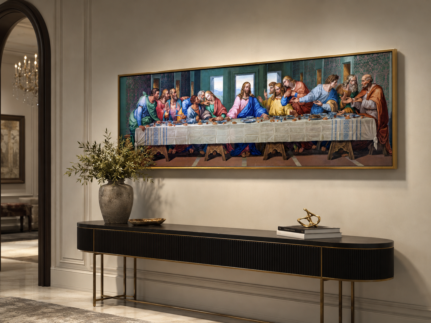 A large framed canvas print of Leonardo da Vinci's Last Supper hangs on a beige wall above a long black console table with gold legs in a styled interior room.