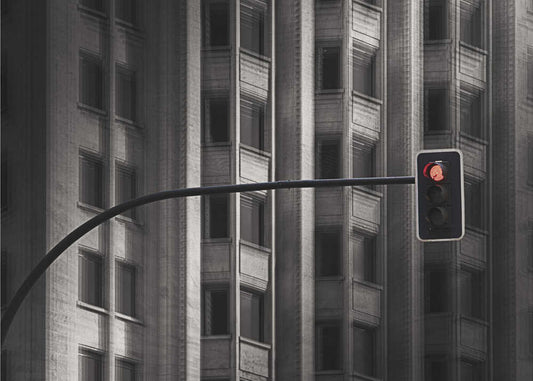 Traffic Light II by Wim Schuurmans, front view of the artwork; a red traffic signal against a dark building facade with repeated vertical windows.