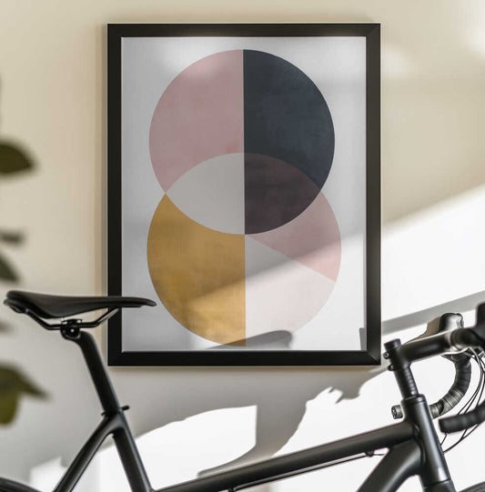 United Spheres by SHANDU, black-framed artwork above a bicycle; two overlapping circles divided into dusty pink, charcoal, ochre and pale sections.